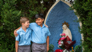 Students hugging in front of a Virgin Madonna statute