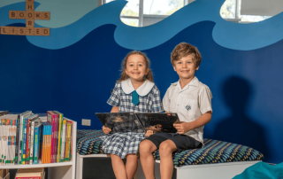 A photo showing two Galilee Catholic Primary School Bondi students reading in the library and on their journey to 2025 NAPLAN results success